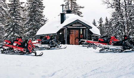 Rote Schneemobile geparkt vor verschneiter Hütte in Schwedisch-Lappland für Singles & Alleinreisende.