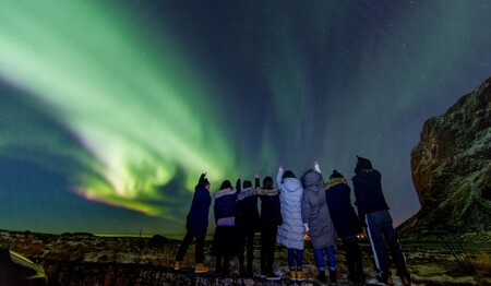 Eine Reisegruppe von Singles & Alleinreisenden beobachtet staunend das grüne Nordlicht am Nachthimmel über Norwegen.