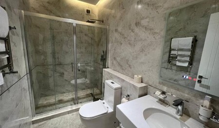 Das hell geflieste Badezimmer im Hotel Pana mit einer großen Glas-Duschkabine und modernem Komfort.