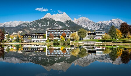 Moderne Hotelanlage direkt am spiegelglatten See vor einer imposanten Bergkulisse im herbstlichen Österreich.