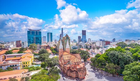Singlereisen in Vietnam: Die Kathedrale Notre Dame vor der modernen Skyline von Ho-Chi-Minh-Stadt.