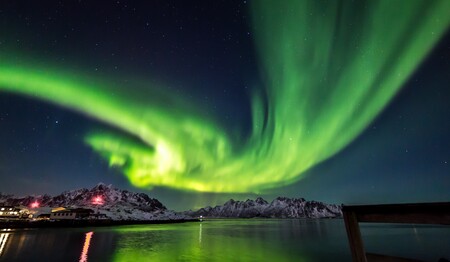 Intensive grüne Nordlichter spiegeln sich im Wasser nahe einer schneebedeckten Bergkette im Urlaub für Singles.