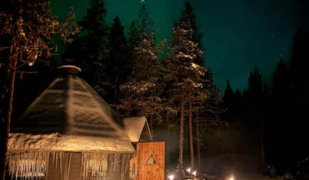 Leuchtende Polarlichter über einer Hütte mit Lagerfeuer in Schwedisch-Lappland für Singles & Alleinreisende.