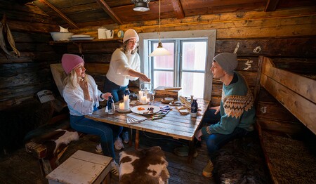 Singles & Alleinreisende sitzen in geselliger Runde in einer urigen Fischerhütte bei regionalen Köstlichkeiten im Norden Norwegens.
