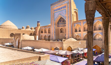 Historischer Markt vor einer prächtigen Medrese mit blauen Mosaiken in der Altstadt von Chiwa in Usbekistan.