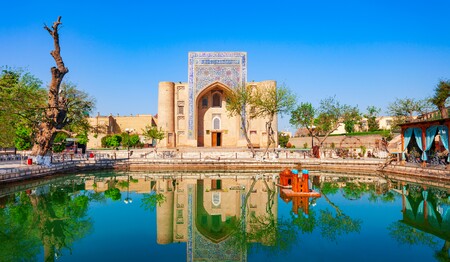 Die historische Nadir-Divan-Begi-Khanaka in Buchara spiegelt sich im zentralen Teich des Labi-Chauz-Ensembles in Usbekistan bei blauem Himmel.