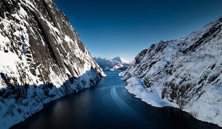 Ein RIB-Boot zieht eine weiße Heckwelle durch das tiefblaue Wasser eines von steilen, schneebedeckten Felswänden gesäumten Fjords.