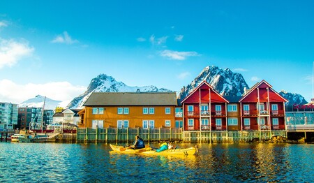 Zwei Teilnehmer einer Singlereise nach Norwegen paddeln im gelben Doppelkajak an traditionellen Rorbuer-Hütten vorbei.