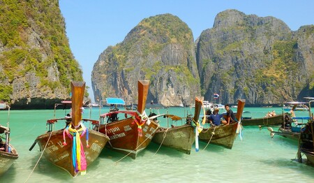 Langboote vor steilen Felsen im türkisfarbenen Meer – typisch für eine Singlereise in Thailand