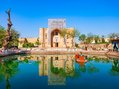 Die historische Nadir-Divan-Begi-Khanaka in Buchara spiegelt sich im zentralen Teich des Labi-Chauz-Ensembles in Usbekistan bei blauem Himmel.