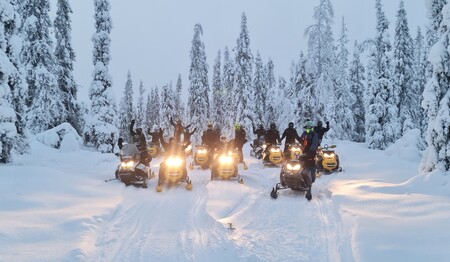 Fröhliche Reisegruppe in Lappland mit Schneemobilen im verschneiten Winterwald für Singles & Alleinreisende.