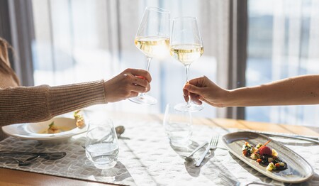 Zwei Personen stoßen beim stilvollen Abendessen im Hotelrestaurant mit Weißweingläsern an – gesellige Momente im Singleurlaub in Österreich.
